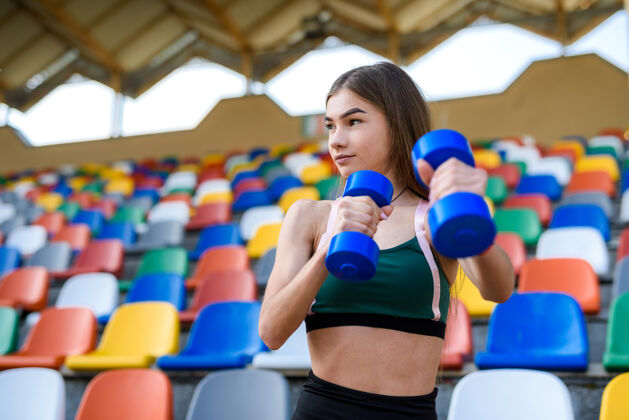 体育场年轻的健身女在城市体育场练习哑铃运动理念运动健康美丽