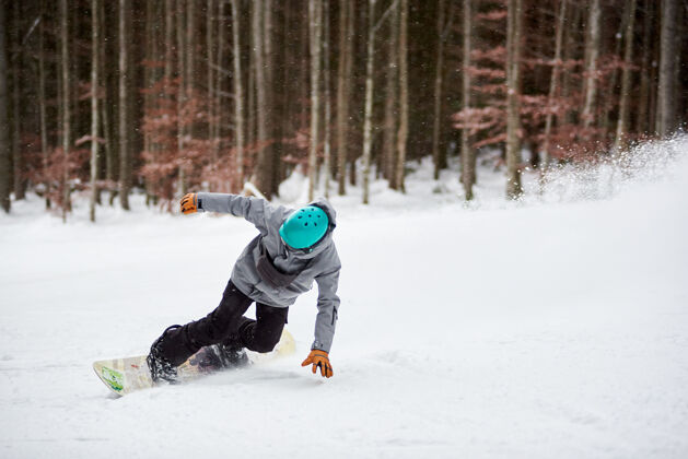 自然戴着蓝色头盔的男子滑雪板运动员 在平坦的积雪覆盖的道路上冒险滑行背景是树干和黑森林粉下降极限