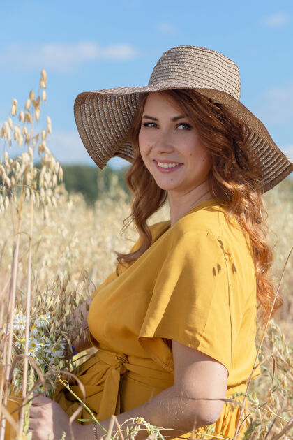人在一个阳光明媚的夏日 一位年轻漂亮的孕妇穿着黄色的裙子 戴着黄色的帽子 走过一片麦田出生天空农村