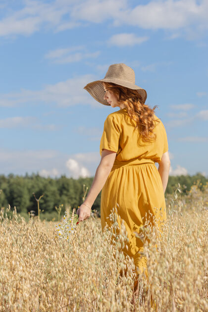 帽子在一个阳光明媚的夏日 一位年轻漂亮的孕妇穿着黄色的裙子 戴着黄色的帽子 走过一片麦田天空父母肖像