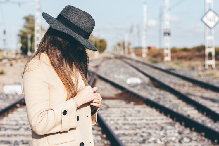 女孩在废弃的铁轨上穿着米色风衣戴着帽子的神秘女人女性时尚沉思