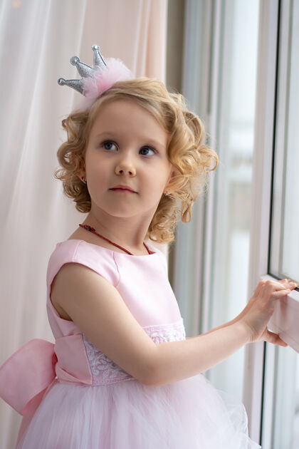 裙子一个穿着粉色裙子戴着皇冠的女孩在窗边微笑宝贝快乐女孩