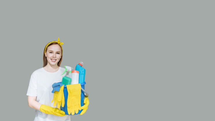 橡皮年轻的微笑女孩与家庭清洁用品上灰色的女佣复制空间女人手套