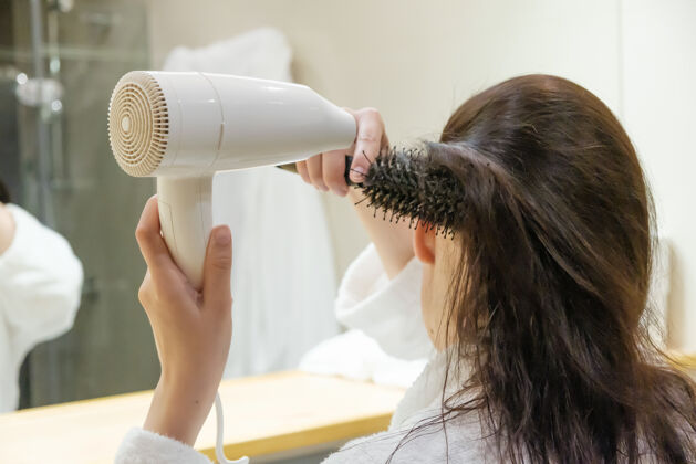 吹风机在浴室里用吹风机吹干头发和用圆毛刷造型的年轻女子女士理发吹风机