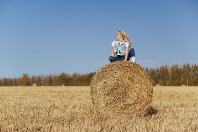 村庄一位年轻漂亮的女村民 穿着牛仔裤 站在地里的一捆干草上女人美丽姿势
