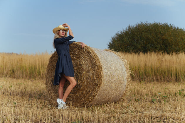 姿势一位年轻漂亮的女村民在一捆干草旁摆出一身衣服玻璃帽子稻草
