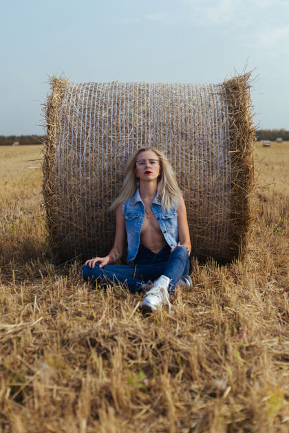 稻草一位年轻漂亮的女村民穿着牛仔裤在一捆干草旁摆姿势草包美丽姿势
