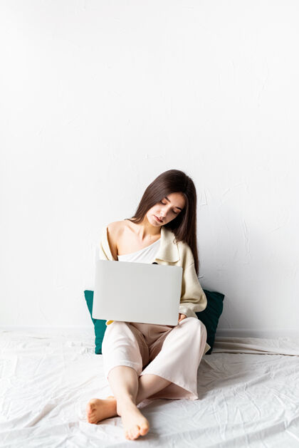 在线美丽的年轻女子坐在地板上做自由项目的笔记本电脑 使用电脑床腿工作场所