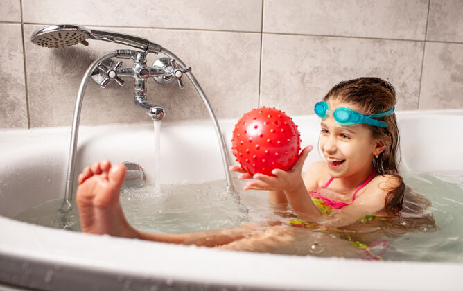 笑声一个穿着泳衣的微笑的小女孩喜欢在洗澡时玩球球清洁液体