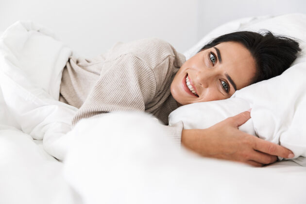 成熟图为30多岁的快乐女人微笑着躺在床上 家里穿着白色亚麻布女士快乐舒适