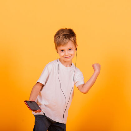 乐趣小男孩戴着耳机听音乐 黄色的背景.儿童耳机里的童话故事小玩意欢呼男孩