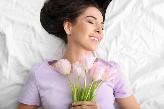 快乐床上躺着一束郁金香的美丽年轻女子国际礼物春天