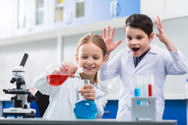 教育你呢疯了一点点精力充沛的男孩一边叫喊一边举手 女孩一边搅拌液体分析玻璃器皿科学