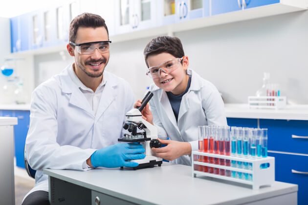 制服专业科学家正派帅哥带着孩子坐在一起 戴着防护眼镜上科学课试剂智能学习