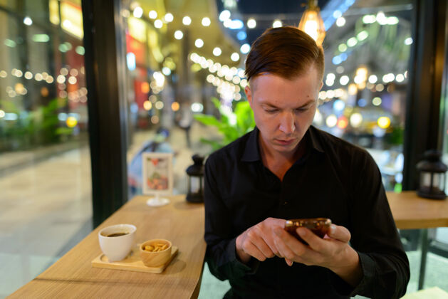 里面年轻英俊的斯堪的纳维亚商人在咖啡店放松的画像连接手机咖啡馆