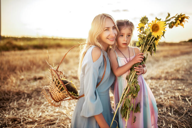 孩子微笑的年轻母亲带着一束向日葵和她可爱的小女儿走在一起阳光童年女人