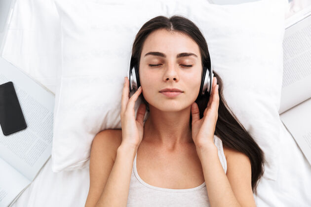 休闲俯视图：一位美丽的年轻女子躺在床上用耳机听音乐床概念小玩意