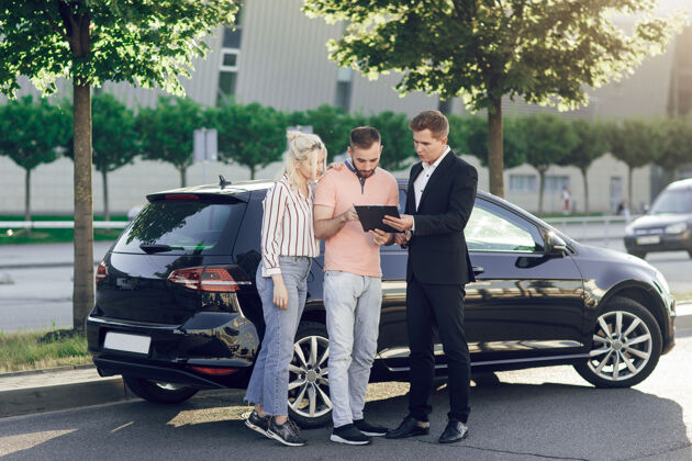 商务男士一个年轻的推销员向顾客展示一辆新车幸福的一对 男人和女人买了一辆新车年轻人签署文件买车展台汽车汽车