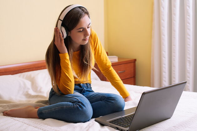 网络空间年轻女子戴着耳机看着躺在床上的笔记本电脑屏幕快乐屏幕房间