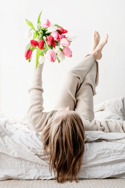 节日幸福的女人穿着睡衣躺在床上 双手捧着鲜艳的郁金香花束花妈妈快乐