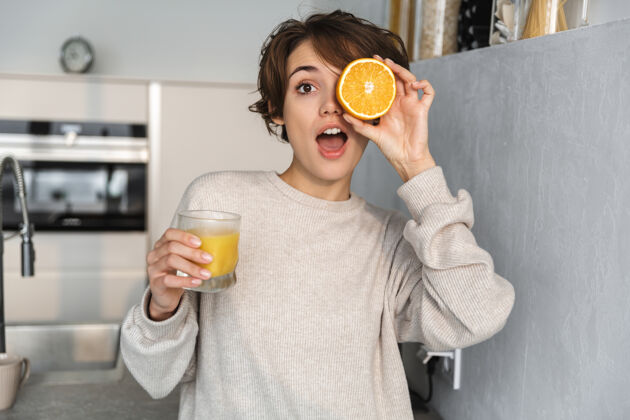 漂亮站在厨房里 手里拿着橙汁和橙子水果的微笑的年轻女子年轻微笑柑橘