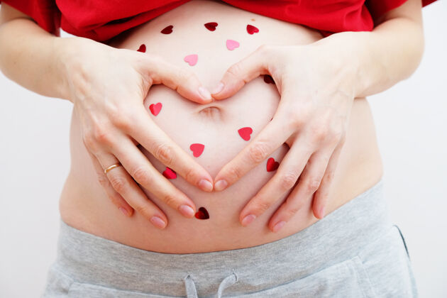 责任孕妇抱着她的手在她的婴儿肿块的心脏形状怀孕的腹部有手指心的象征母性观念情人节的概念肥料医疗碰撞
