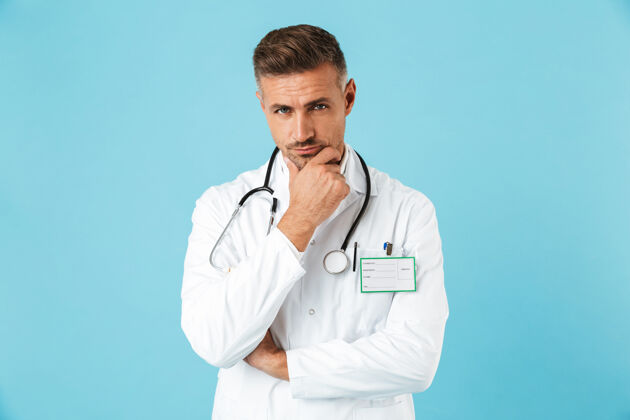 职业穿着白色制服 戴着听诊器的白人医生的画像 孤立地站在蓝色的墙上心脏病专家情绪中年