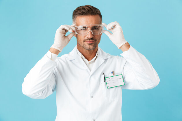 保护自信的男医生穿着制服戴着眼镜孤立地站在蓝色的墙上职业制服医生