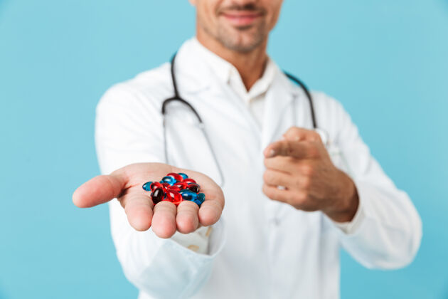 男人医学专家身穿白大褂 手捧药丸 孤立地站在蓝色墙壁上的照片医疗治疗职业