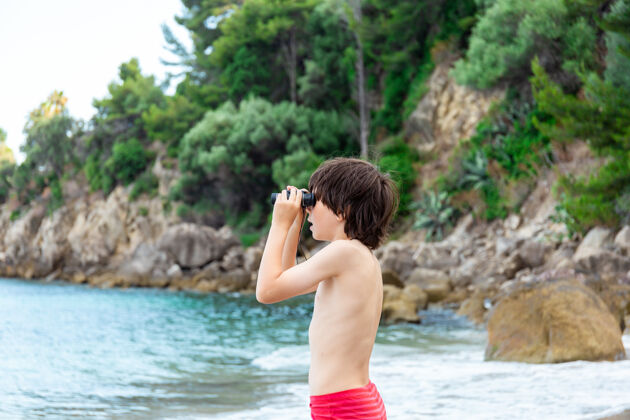 玩一个小男孩呆在海边的海滩上 用望远镜看东西海军男性年轻