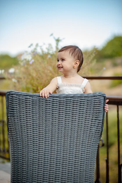 有趣可爱的女婴穿着白色的裙子站在草椅上大笑的垂直镜头头发站婴儿