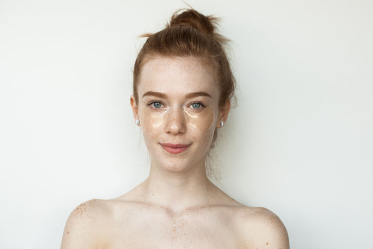 时尚满脸雀斑的红发白种女人戴着水凝胶眼罩 赤裸着肩膀站在白墙上姿势卫生面部