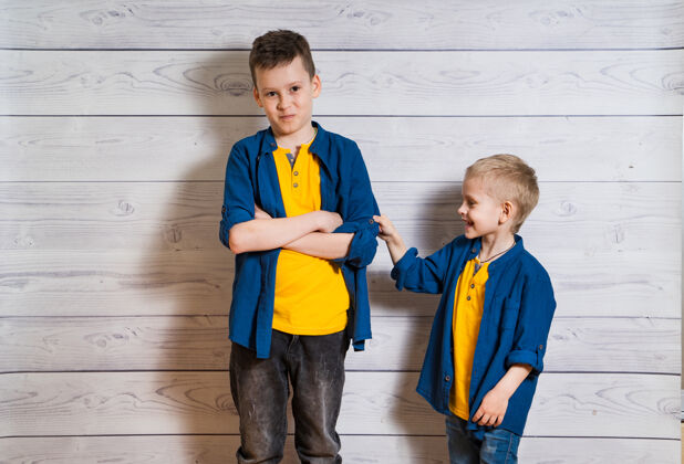 相机两个穿着蓝色衬衫和黄色t恤的快乐男孩一起摆姿势兄弟快乐年轻