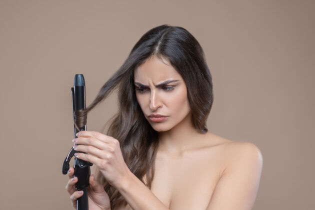 严格卷曲卷发认真的一个年轻的黑发女人 光着肩膀 用黑色卷发棒卷发裸体长发头发