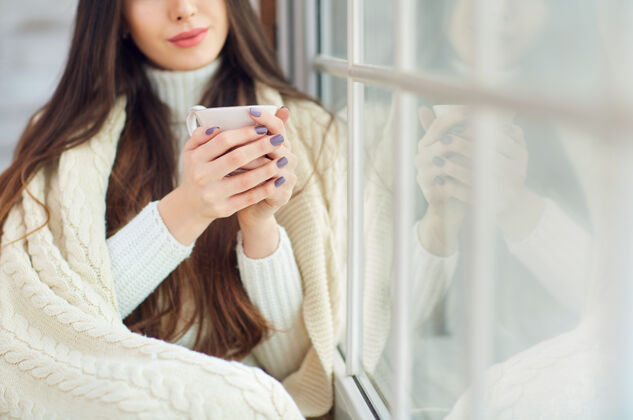 人冬天 女孩在窗前喝着一杯咖啡漂亮圣诞树坐着