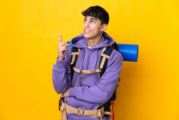 运动一个年轻的登山者背着一个大背包 越过孤立的黄色墙壁 提出了一个伟大的想法西班牙裔年轻手
