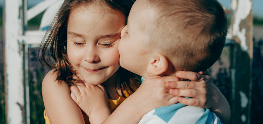 学前班一个白人金发男孩和他的妹妹在夕阳下亲吻和拥抱的特写镜头日落表达朋友