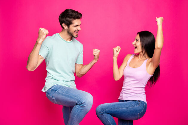 微笑冠军夫妇的资料照片男男女女举起拳头庆祝惊人成就穿休闲服隔离亮粉色背景牛仔裤是的女孩