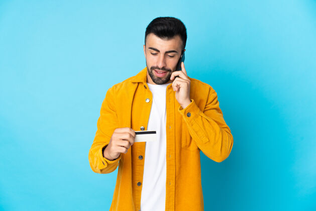 支付一个白人男子在孤立的蓝色背景下用手机用信用卡购物成人男性购物