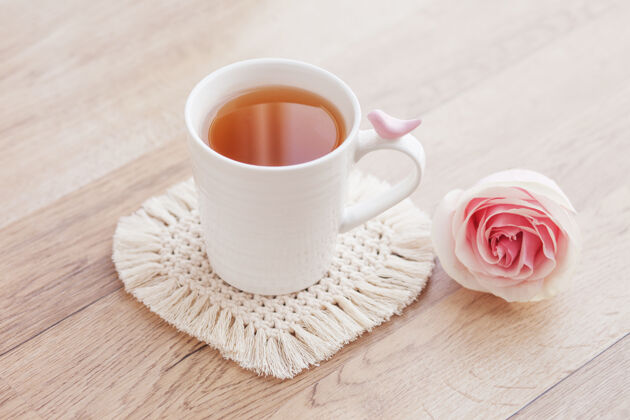 茶Macrame手工制作爱好茶在一个杯子里放着白色的马克莱姆杯垫 放在木桌上放着玫瑰顶部结纱