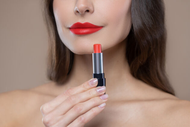 长发红色是趋势下降女人脸上的一部分 鲜艳的唇膏在美丽的嘴唇和手上裸体感觉米色背景