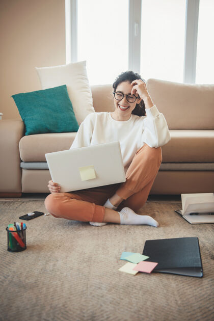 千禧一代笑容可掬的白种女人正在客厅的地板上用笔记本电脑上在线课坐姿爱情工作