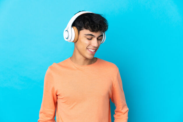 好年轻人在孤独的蓝色背景下听音乐年轻耳机生活方式