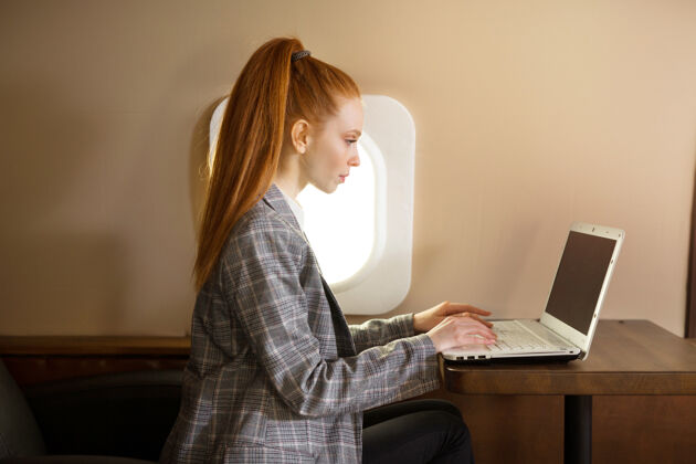 商务女性一位红发美女在机舱里拿着笔记本电脑旅行交通在线