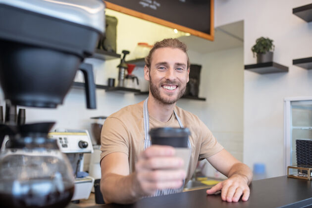 建议咖啡师咖啡厅柜台上留着胡须的年轻男咖啡师礼貌地端出一杯咖啡咖啡馆男人准备