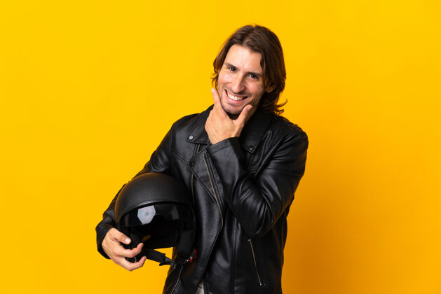 男人一个戴着摩托车头盔的男人被隔离在黄色的墙上 快乐而微笑头盔乐趣自信