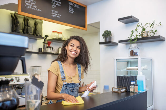 舒适工作 年轻咖啡馆快乐的黑发女人站在一边看着擦吧台焦点女士工作