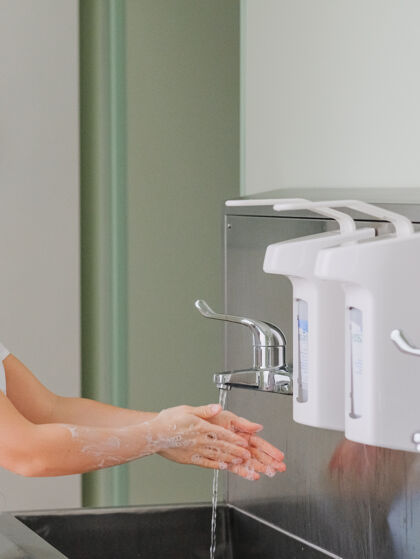 肥皂女人的手是用肥皂在不锈钢水槽上的喷水器下洗的水龙头清洗抗菌
