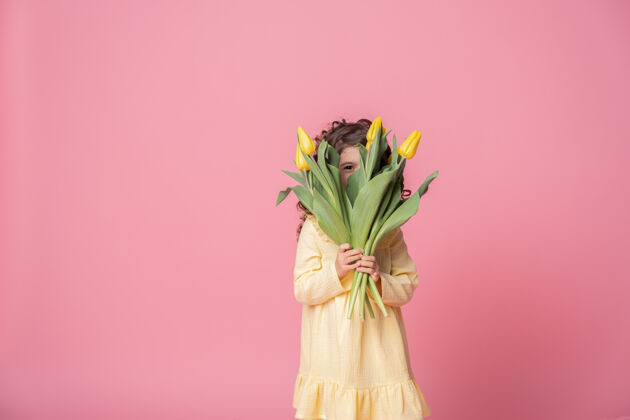 活动粉红工作室里一个穿着黄色连衣裙的微笑女孩背景欢快郁金香花束快乐的孩子童年花春天