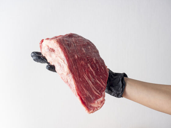 晚餐一只戴着黑手套的手拿着一块鲜生的大理石牛肉 背景很浅持有厨师有机